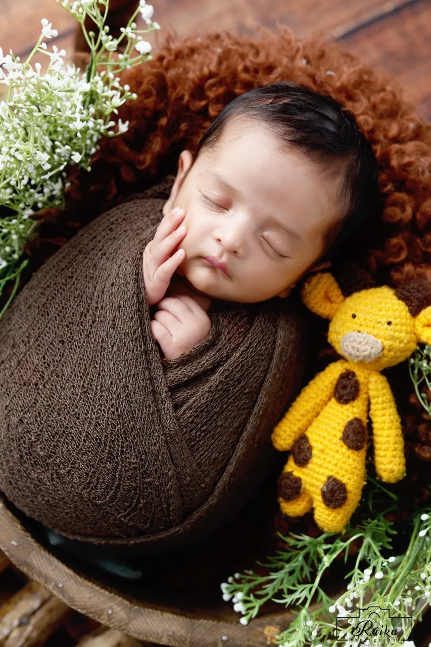 Newborn wrapped in red, resting among white flowers